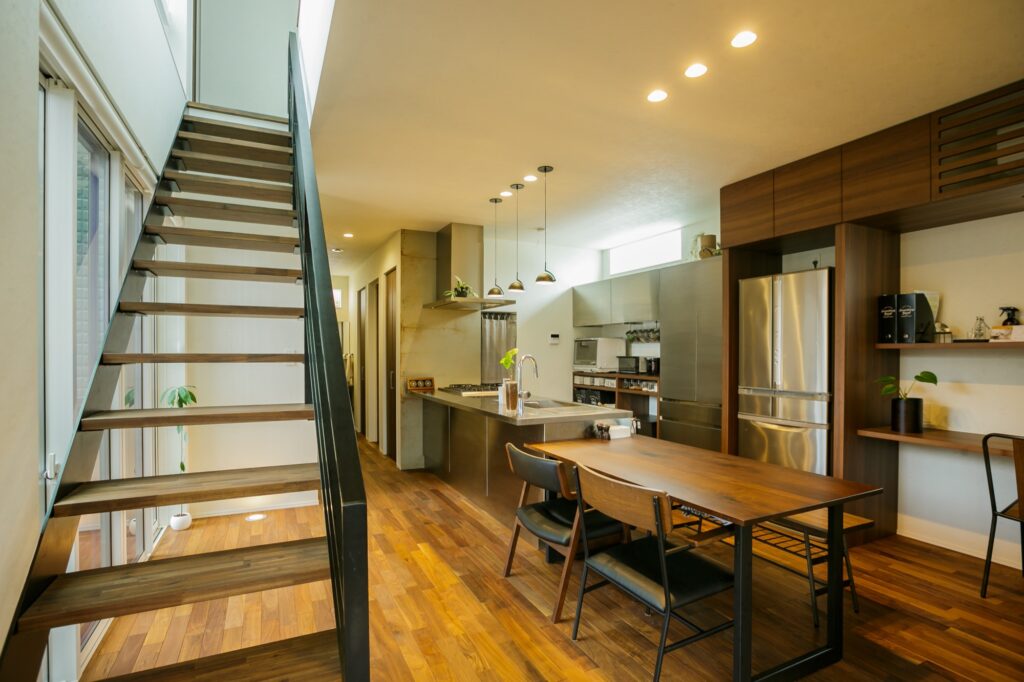 木製踏板と黒い手すりのスケルトン階段が印象的なモダンな空間。と木目調のダイニングテーブルが調和したキッチン